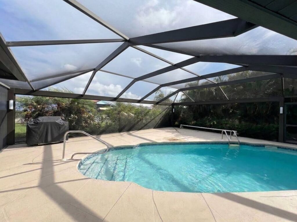 Black pool cage over the pool after a panoramic picture-window screen conversion, with a clear view of the backyard