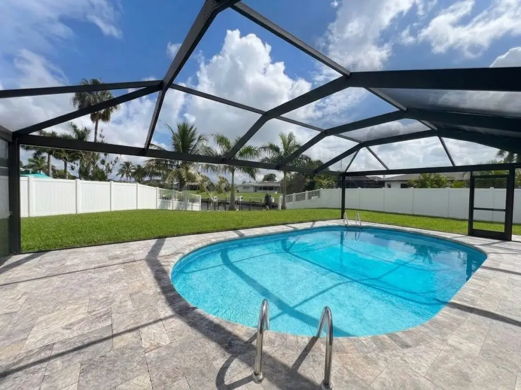 Black pool cage over the pool after a panoramic picture-window screen conversion, with a clear view of the backyard