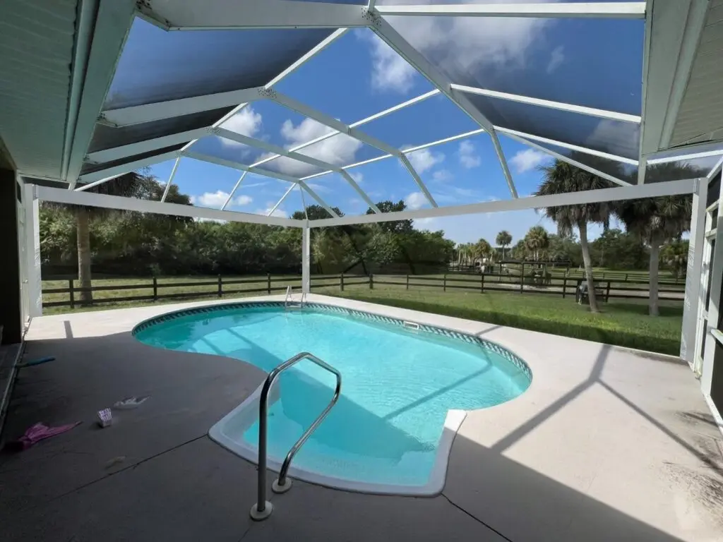 White pool cage over the pool after a panoramic picture-window screen conversion, with a clear view of the backyard
