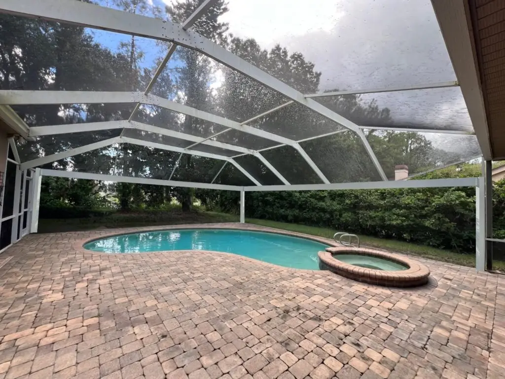White pool cage over the pool and spa after a panoramic picture-window screen conversion, with a clear view of the backyard