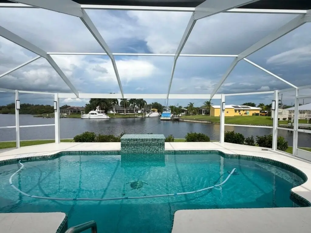 White pool cage over the pool after a panoramic picture-window screen conversion, with an open waterfront view