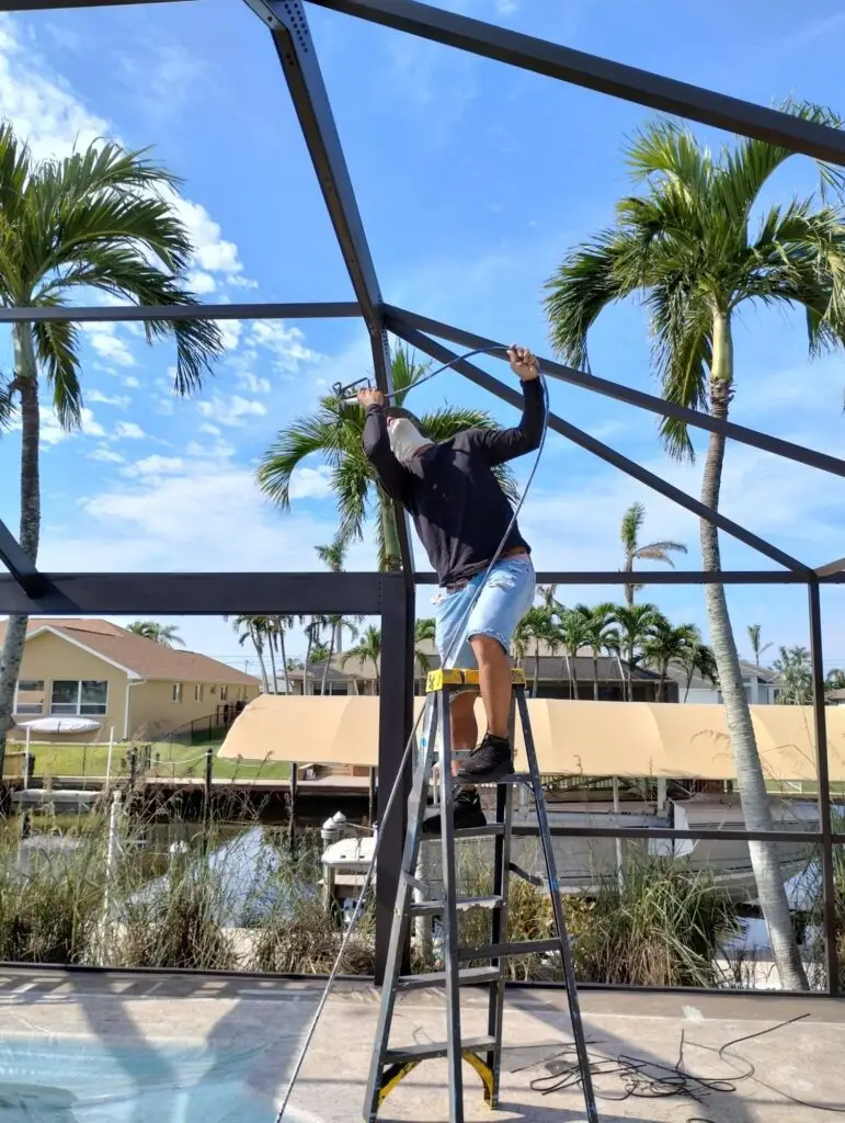 Painter on a ladder painting a bronze pool cage frame by the water