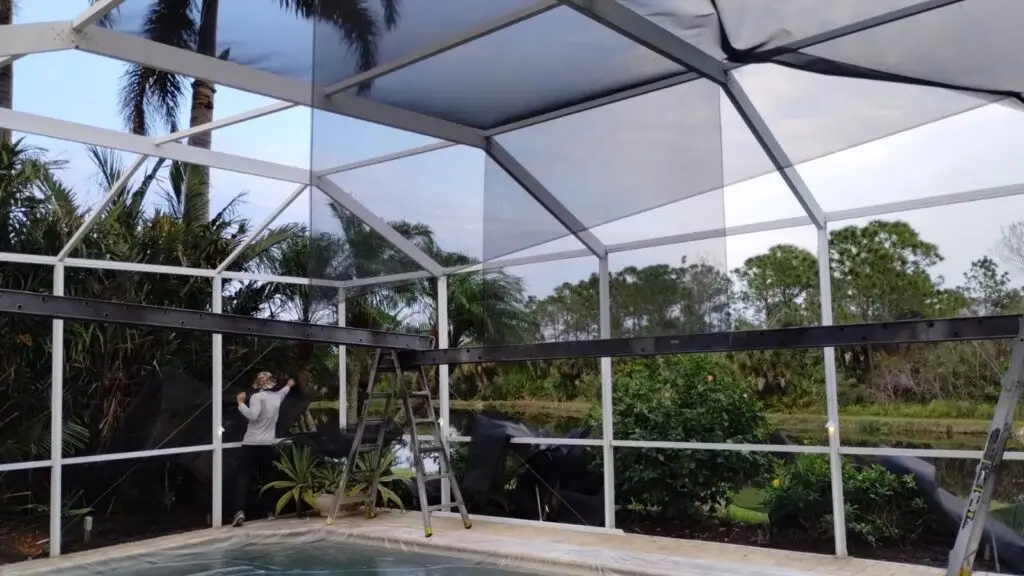 Installer fitting new screen on a bronze pool cage after painting