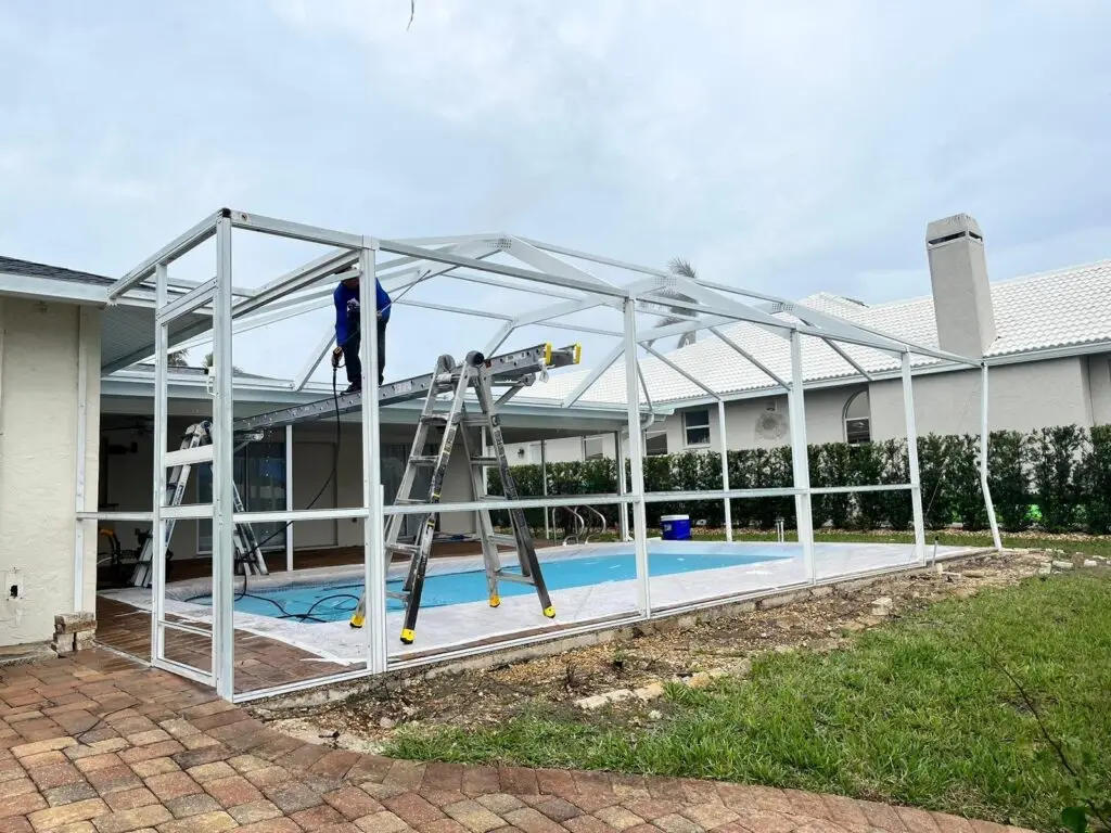 White pool cage frame freshly painted, painter on a ladder by the pool