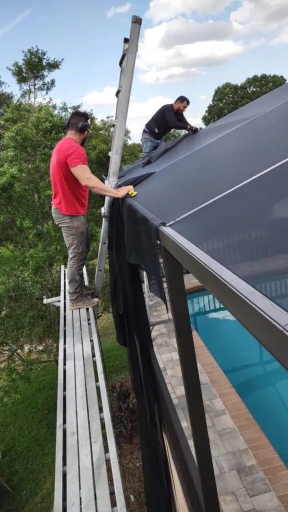 Installer rolling new screen onto a pool cage roof panel