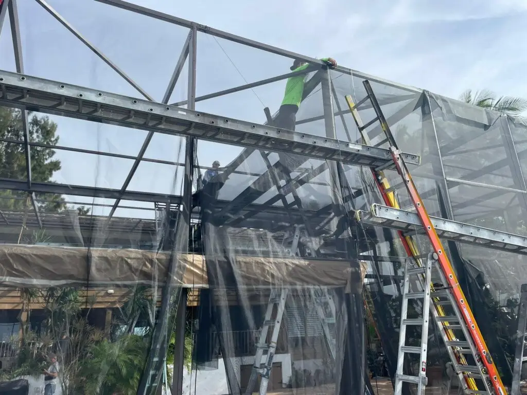 Installer on a ladder securing new screen panels on a pool cage