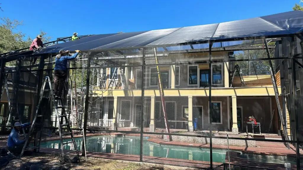 Crew installing new screen on a pool cage roof over the pool